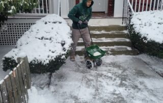 Worker spreading ice melt on snowy sidewalk and steps for safe entry