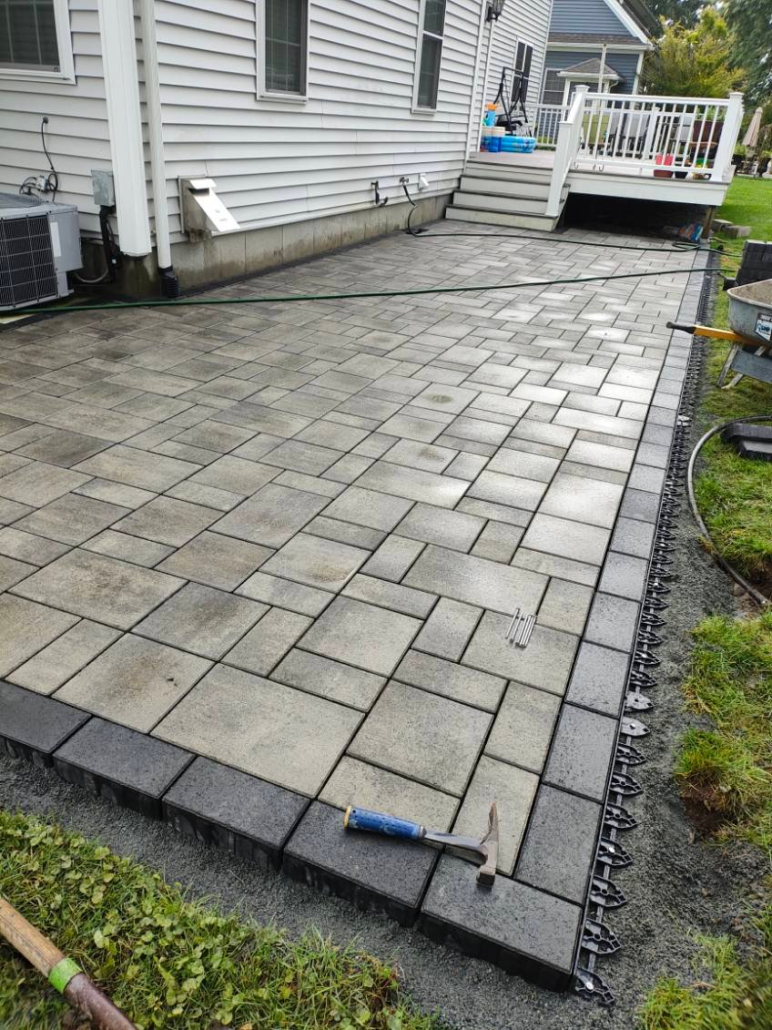 Newly installed stone paver patio with dark border beside residential deck