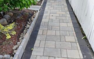 Newly installed stone paver walkway with dark border leading to home entrance
