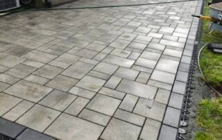 Newly built stone paver patio with dark edging beside residential home