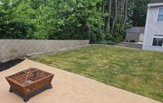 Freshly mowed backyard lawn with fire pit on patio and wooden fence border