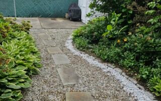 Gravel pathway with stepping stones and bordered garden plants in backyard