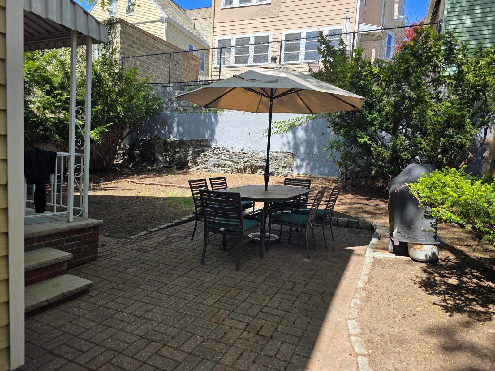 Brick patio with outdoor dining set and umbrella in landscaped backyard