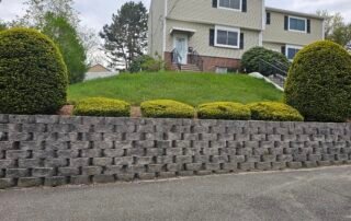 Residential retaining wall with neatly trimmed hedges and green lawn